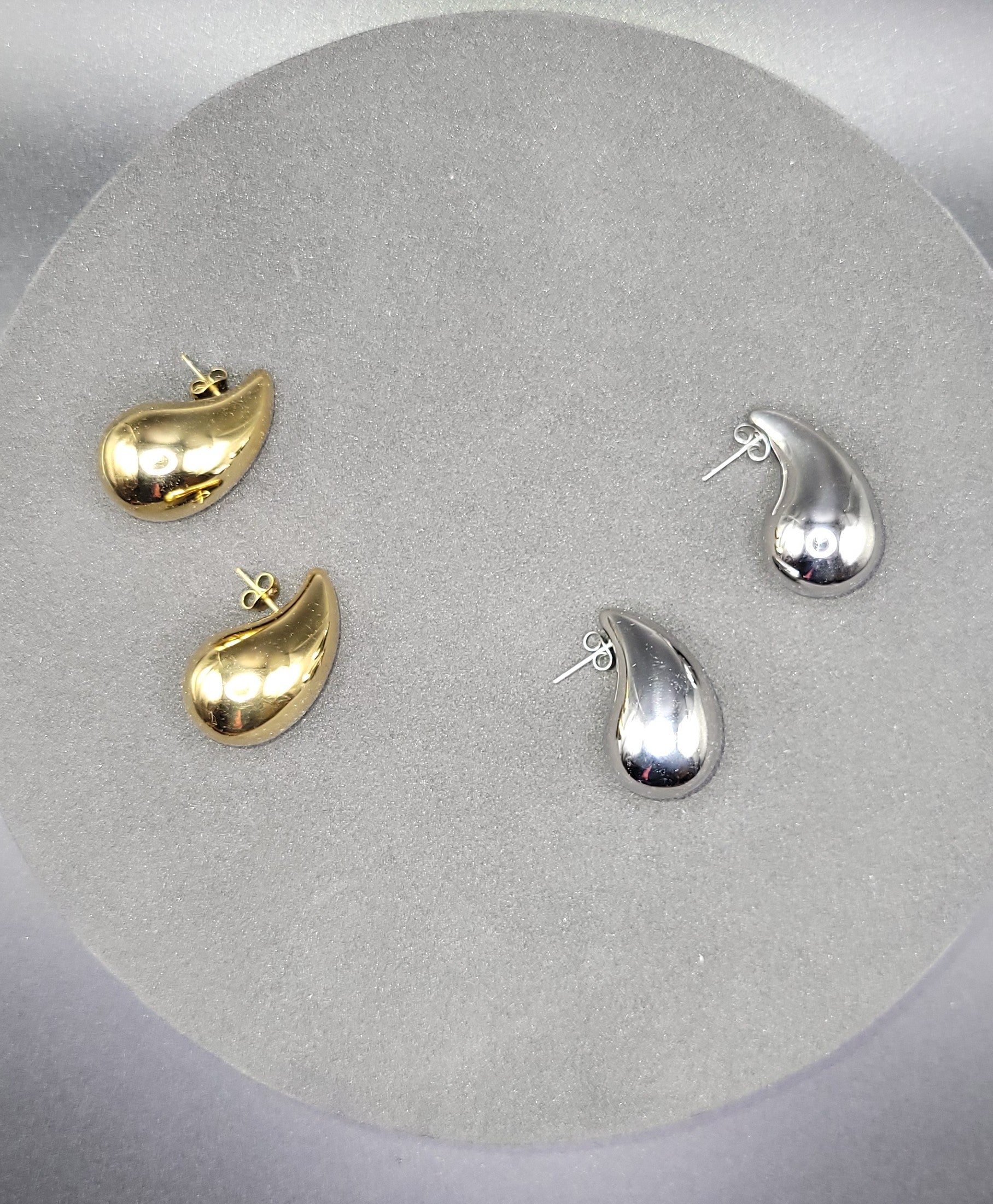 A pair of raindrop-shaped earrings in two colors, gold on the left and silver on the right.