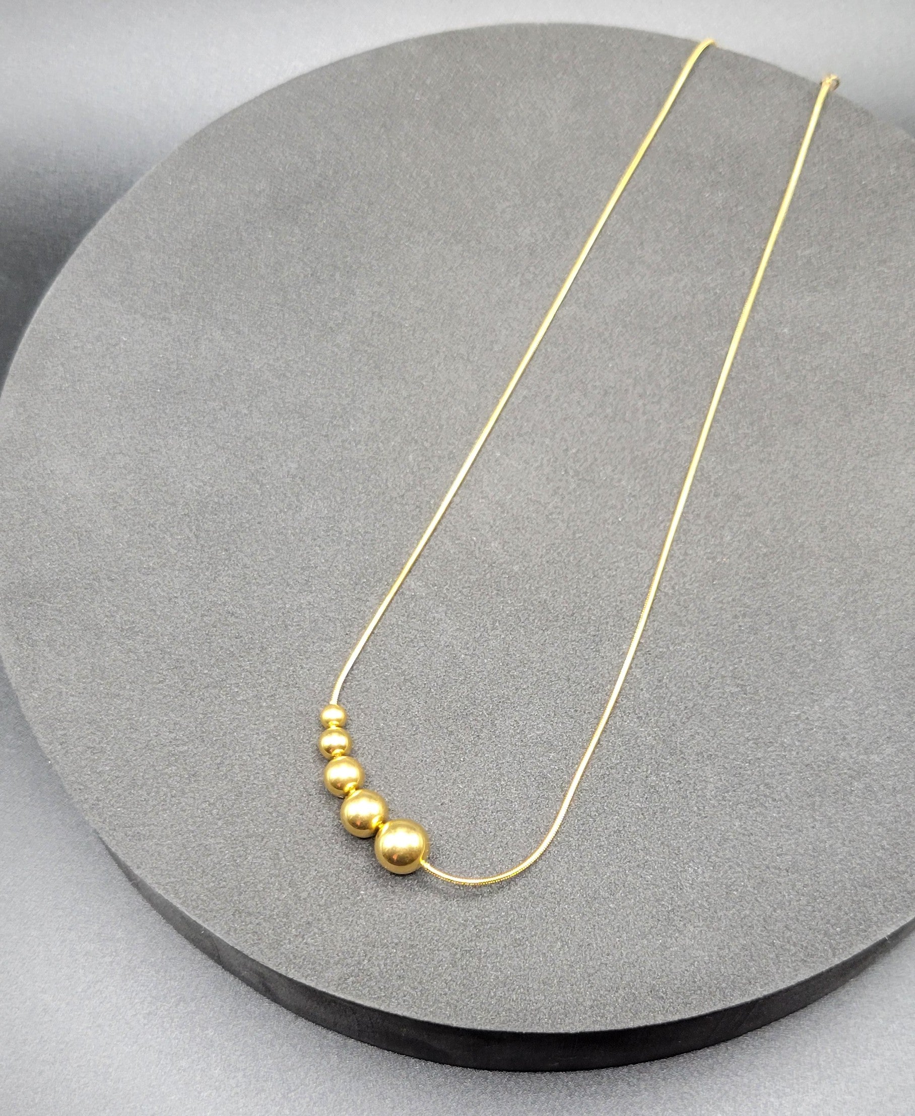 A gold-plated snake chain necklace with graduated beaded design.