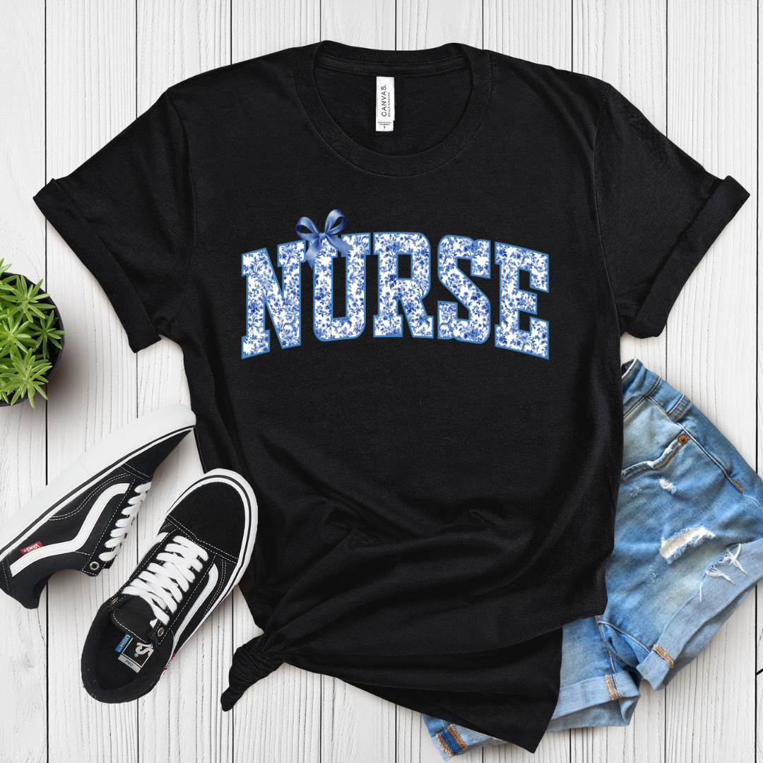 Black t-shirt with 'NURSE' printed in blue on a wooden surface with sneakers and shorts.