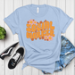 Light blue t-shirt with 'Social Worker' text and flowers on a wooden surface with sneakers and shorts.