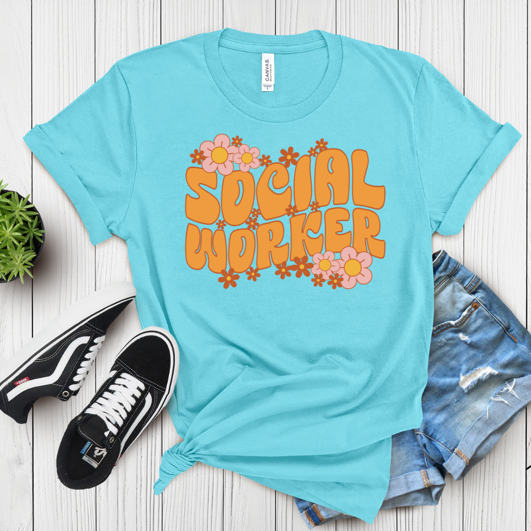 Blue t-shirt with 'Social Worker' text and flowers on a wooden surface with sneakers and shorts.