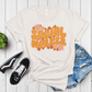 White t-shirt with 'Social Worker' text and flowers, paired with sneakers and jeans on a wooden surface.