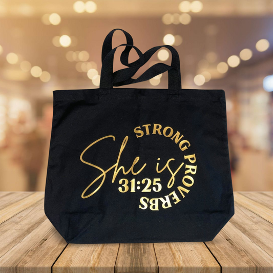 A black tote bag with the text 'She is PROUD' written in gold.