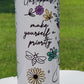 Tumbler with motivational quote and floral designs on a white surface with greenery in the background